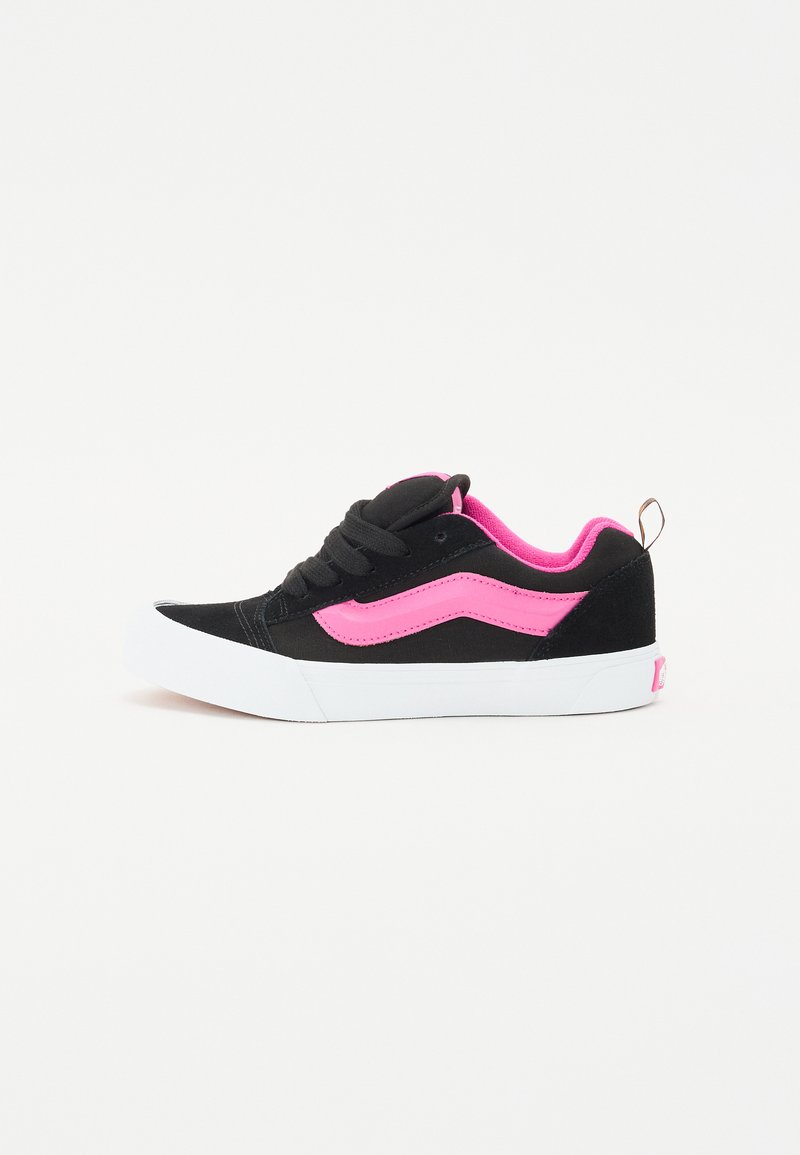 Black suede sneakers with pink accents and white rubber sole. Features a fabric tongue, lace-up design, and a pull tab at the heel.