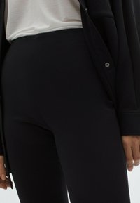 Mustat leggingit, jotka on valmistettu joustavasta kankaasta, jossa on sileä pinta. Yhdistettynä vaaleansävyiseen, löysästi istuvaan puseroon ja tummanväriseen bleiseriin.