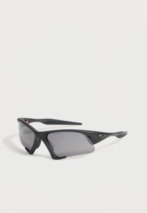Lunettes de sport noires avec verres gris enveloppants et branches légèrement courbées, présentées sur un fond clair uni.