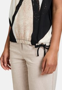 Loose-fitting top with black, cream, and beige abstract design; features a cinched hem with a black drawstring. Light beige textured pants.