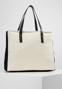 Duża torba na ramię z kremowym płótnem i czarnymi zamszowymi bokami. Czarną skórzaną rączką, prostokątny kształt, minimalistyczny design.