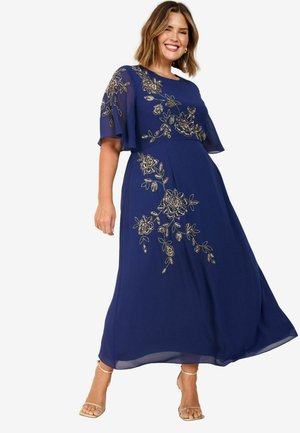 Navy blauwe maxi-jurk met korte vlindermouwen, voorzien van gouden bloemenborduursels langs het lijfje en de vloeiende rok. Glad stofoppervlak.