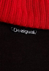 Rode geribbelde gebreide stof gaat over in een zwarte, gestructureerde brei, met een zilveren "Desigual" logo label op het zwarte gedeelte.