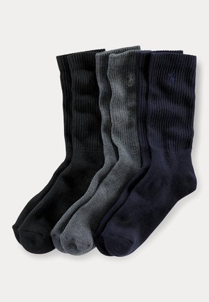 Vier Paar gerippte Crew-Socken in Schwarz, Dunkelgrau und Marineblau, nebeneinander auf hellem Hintergrund angeordnet.