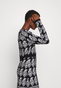 Robe à motifs noirs et blancs présentant un design de feuilles, manches longues et silhouette ajustée. Le tissu semble doux avec des accents côtelés.
