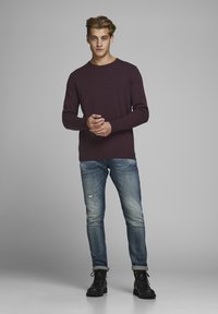 Suéter de cuello redondo burdeos, tejido ligero, combinado con jeans azules desgastados con desgastados. Botas negras de cordones completan el conjunto.