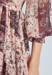 Vestito con motivi floreali nei toni di rosa, marrone scuro e crema. Presenta delle pieghe e maniche a sbuffo, realizzato in stoffa leggera e testurizzata.