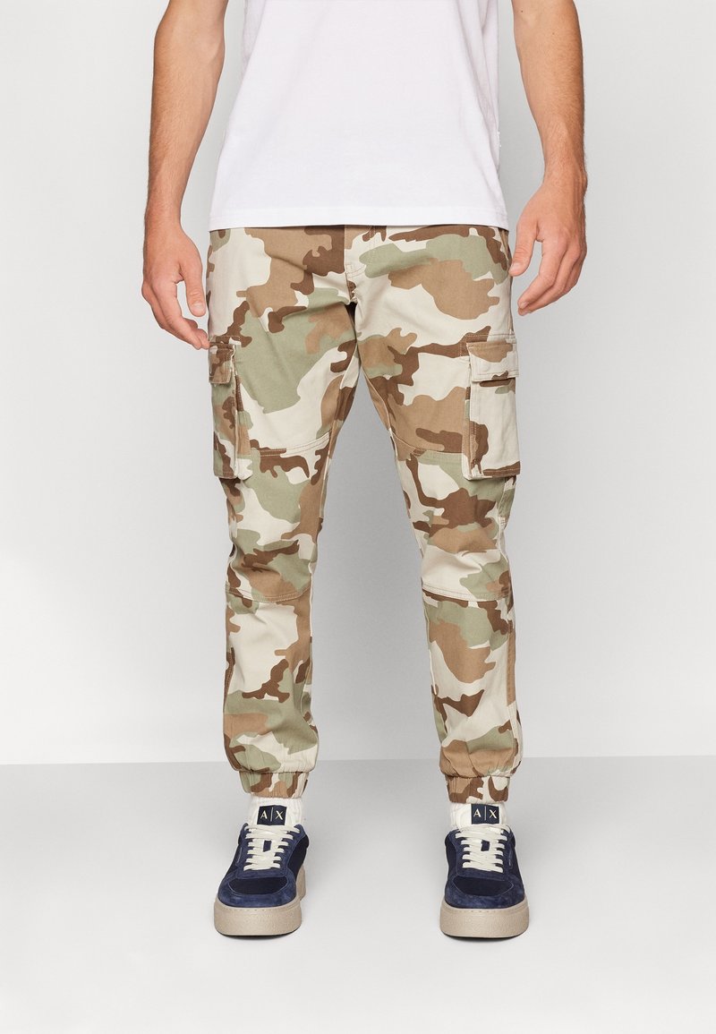 Camouflage cargobroek in beige, groen en bruine tinten. Kenmerken zijn onder andere elastische boorden, meerdere zakken en een relaxte pasvorm.
