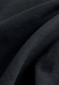 Tejido negro de punto con textura de tejido visible, mostrado en primer plano con pliegues suaves y sombras que resaltan los detalles del material.