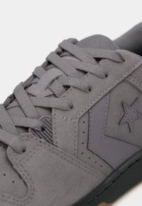 Grå semsket sneakers med en teksturert overflate, kontrasterende lærdetaljer, flate lisser, gummisåle og stjerneemblemet på siden.