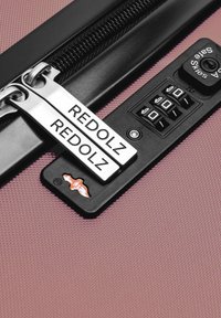 Maleta rosa con cremallera, cerradura de combinación negra y dos tiradores de cremallera plateados grabados con "REDOLZ" en una superficie texturizada.