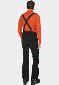 Schwarze Skihosen mit verstellbaren schwarzen Trägern und Reißverschlusstaschen, kombiniert mit einem orangefarbenen Langarmoberteil mit glatter Textur.