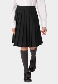 Falda negra plisada con una cinturilla suave, combinada con calcetas grises hasta la rodilla y zapatos de charol negros.