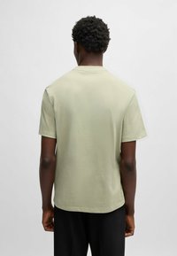 T-shirt a maniche corte di un leggero verde oliva, realizzato in cotone. Presenta un colletto girocollo e un orlo dritto. Texture liscia, design minimal.