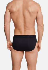Slip da uomo nero con texture a coste e cintura elastica, che mostra una vestibilità aderente, visti da dietro. Nessun ulteriore dettaglio visibile.