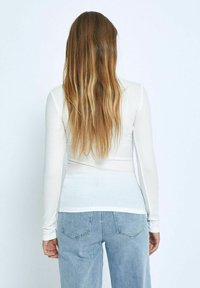 Witte lange mouwen top met een aansluitend ontwerp en een gladde textuur, gecombineerd met lichtblauwe jeans met achterzakken.