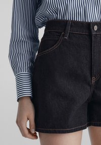 Tummansiniset denimshortsit, joissa korkeavyötärö, oranssit saumat ja etutaskut. Yhdistetty sinivalkoraidalliseen pitkähihnaiseen paitaan.