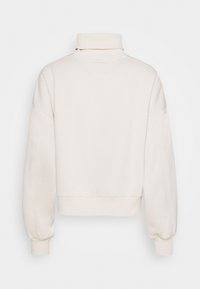 Krémový rolák s dlouhými rukávy a žebrovanými manžetami, zobrazený zezadu na bílém pozadí.