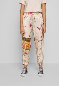 Blommönstrade, lätta byxor i krämfärgad nyans, med elastisk midja och muddar, prydda med olika livfulla mönster på tyget.