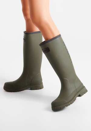 Bottes de pluie vertes en caoutchouc, hautes jusqu'aux genoux, avec des semelles texturées et des bordures noires. Présente une étiquette de marque sur le haut de la tige. Matériau lisse et imperméable.