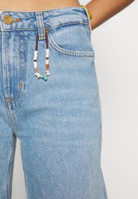 Lichtblauwe spijkerbroek met een rechte pasvorm. Voorzien van een kleurrijke kralenketting bevestigd aan de voorkant van de tailleband. Klassiek ontwerp met vijf zakken.