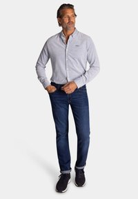 Lichtgrijs overhemd met lange mouwen, gecombineerd met donkerblauwe jeans en zwarte sneakers; eenvoudig ontwerp, geen zichtbare patronen of accenten.