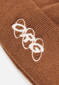 Gorro de malha castanho com um padrão texturizado. Apresenta um logótipo bordado em branco em design circular. Tecido macio e flexível.
