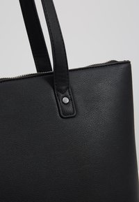 Sac fourre-tout en cuir noir texturé avec double poignée et fermeture éclair argentée visible le long du bord supérieur.