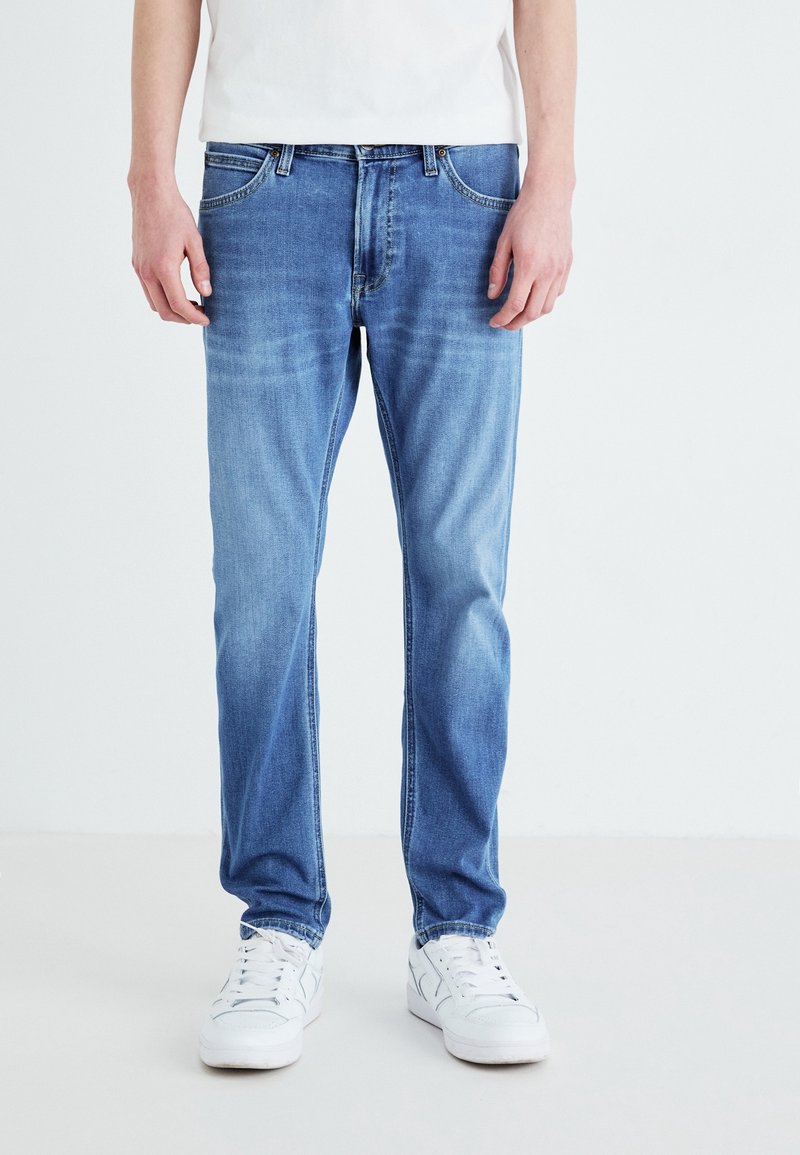 Ljusblå denimjeans med rak passform, blekt utseende, femfickorsdesign och metalldetaljer, bärs med vita sneakers.