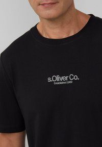 Zwarte katoenen t-shirt met een ronde hals en korte mouwen, voorzien van een grijs geborduurd logo met de tekst "s. Oliver Co. Opgericht in 1969."