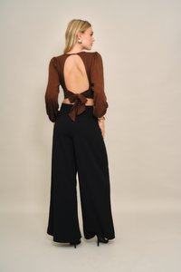 Brauner Langarm-Top mit offenem Rücken und Schleifendetail; kombiniert mit schwarzen, weit geschnittenen Hosen. Glatter Stoff und figurbetonte Silhouette.