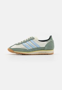 Herresneaker med en lysegrå lærsoverdel, grønne semskede detaljer, blå tre-striper, en strukturert gummisåle og kremfargede snøringer.