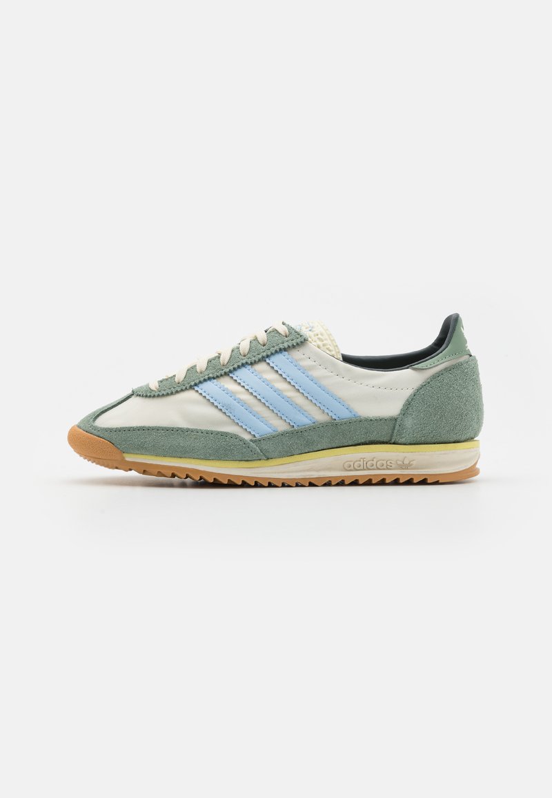 Herresneaker med en lysegrå lærsoverdel, grønne semskede detaljer, blå tre-striper, en strukturert gummisåle og kremfargede snøringer.