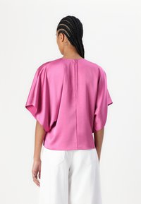 Kortermet, lys rosa bluse laget av sateng med en avslappet passform, som har rund hals og lukking bak. Myk tekstur, glatt overflate.