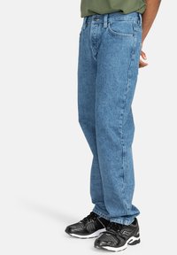 Hellblaue Jeans im geraden Schnitt. Verfügt über fünf Taschen, einen Metallknopfverschluss und eine subtile, ausgewaschene Textur. Kombiniert mit schwarzen Sneakers.
