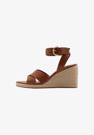 Brown leather wedge sandals with crisscross straps and a buckle ankle strap. Jute-wrapped wedge heel with a textured finish.
