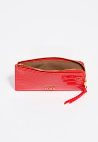 Cartera roja con textura de cocodrilo y cierre de cremallera, acabado liso, herrajes dorados y forro interior marrón. Cuenta con una correa para la muñeca para facilitar su transporte.