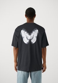 Black cotton t-shirt featuring a large white butterfly graphic on the back. Short sleeves and relaxed fit with a round neckline.