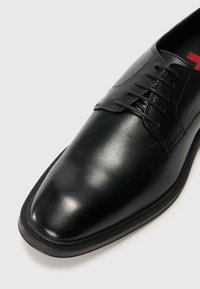 Zwarte leren dress shoe met een gladde afwerking, vetersluiting, ronde neus en een contrasterende gestructureerde zwarte zool. Opvallend logo detail aanwezig.