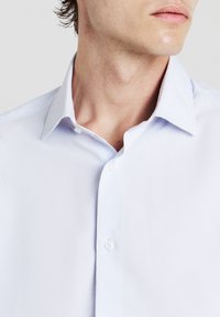 Hellblaues Hemd mit strukturiertem Kragen, dezentes Nadelstreifenmuster und Knopfverschluss. Baumwollmischgewebe, glatte Textur.