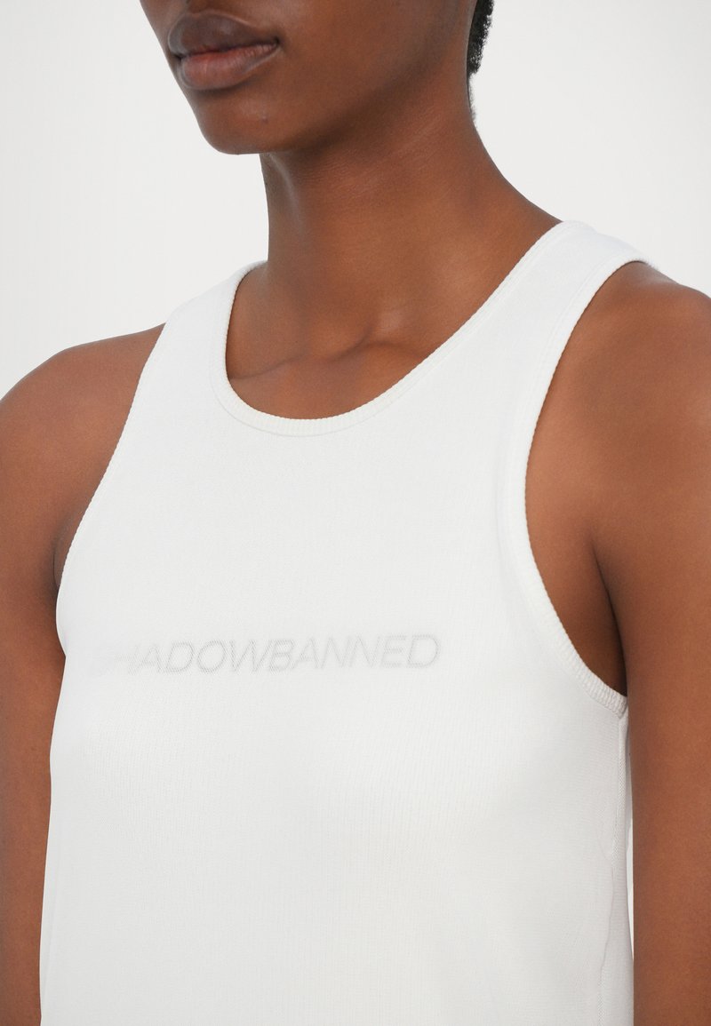 Camiseta sin mangas de canalé blanca con un escote redondo y un sutil texto "SHADOWBANNED" en un tono más claro en el pecho.