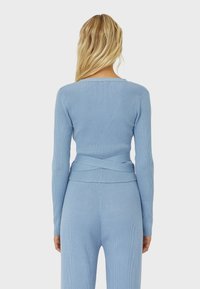 Hellblaues, geripptes Langarmoberteil mit einem V-förmigen Rücken und gekreuzten Details, aus einem weichen, dehnbaren Material.