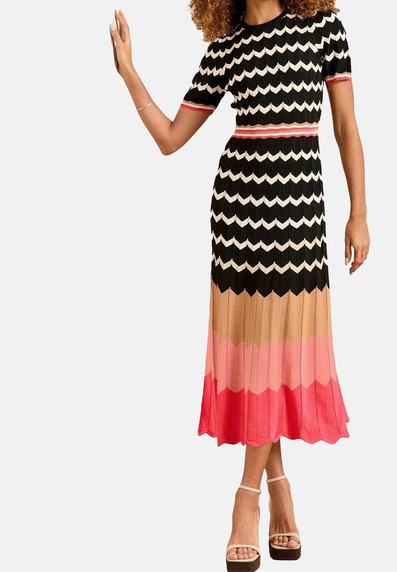 Robe en maille avec un motif chevron en noir, blanc, corail et rose, composée d'un haut ajusté et d'une jupe plissée évasée.