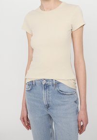 Camiseta de rayas beige con mangas cortas, escote redondo y ajuste ceñido al cuerpo, combinada con jeans de talle alto de color azul claro.