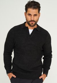 Schwarzer Strickpullover mit Kragen, der ein texturiertes Muster sowie Rippbündchen und Saum aufweist. Leichtes Material, lässiger Stil.