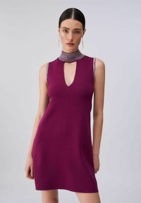 Robe sans manches magenta avec une encolure en œillet et un col montant orné de détails argentés. Texture en maille lisse, longueur au-dessus du genou.