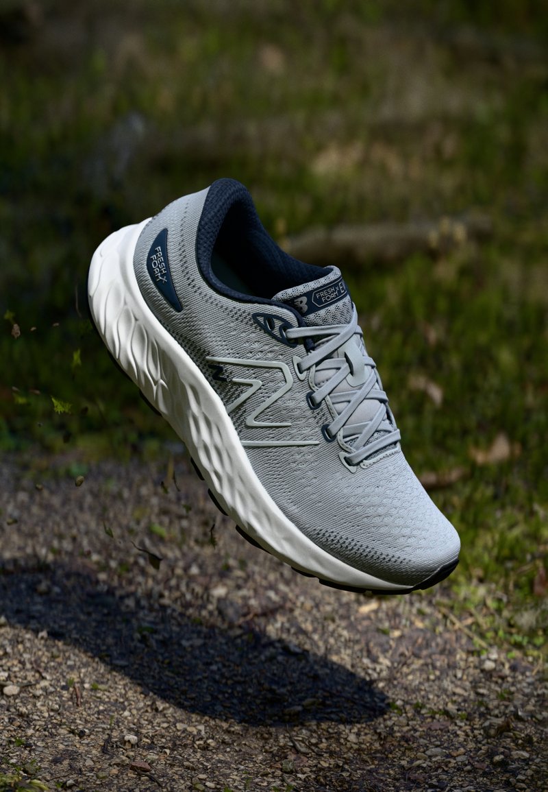 Gray athletic shoe with a textured upper, contrasting dark interior, white midsole, and gray laces. Features branding on the side and tongue.