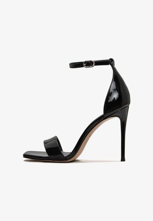 Czarne lakierowane sandały na wysokim obcasie z otwartym przodem, z paskiem na kostce i smukłym, błyszczącym wykończeniem. Posiadają wąski obcas w stylu stiletto.