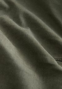 Soft olive green fabric with fine ribbed texture and gentle folds, showing a stitched seam on the lower right side.