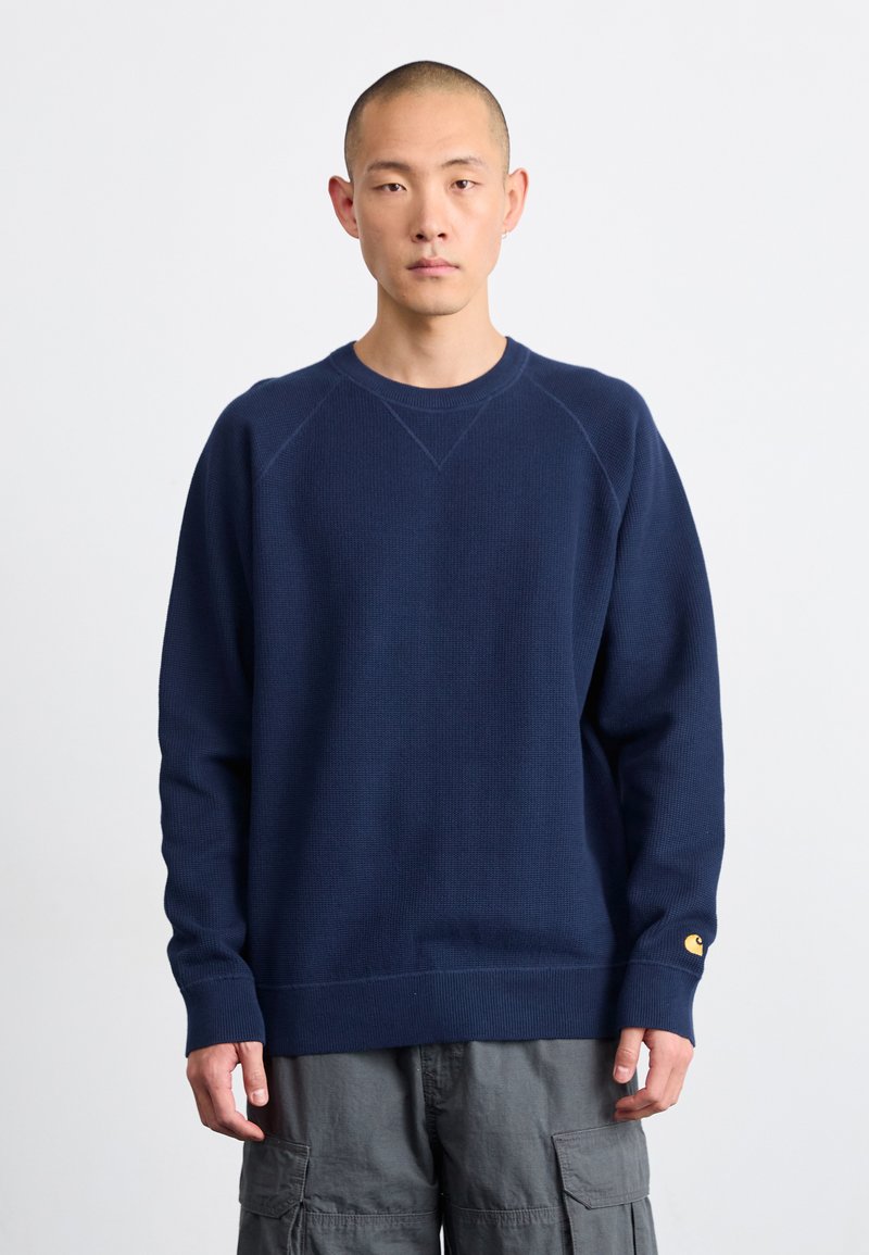 Marineblauwe gebreide sweatshirt met geribbelde ronde hals, manchetten en onderrand. Voorzien van een klein geel logo op de linker mouw. Textuurstof.